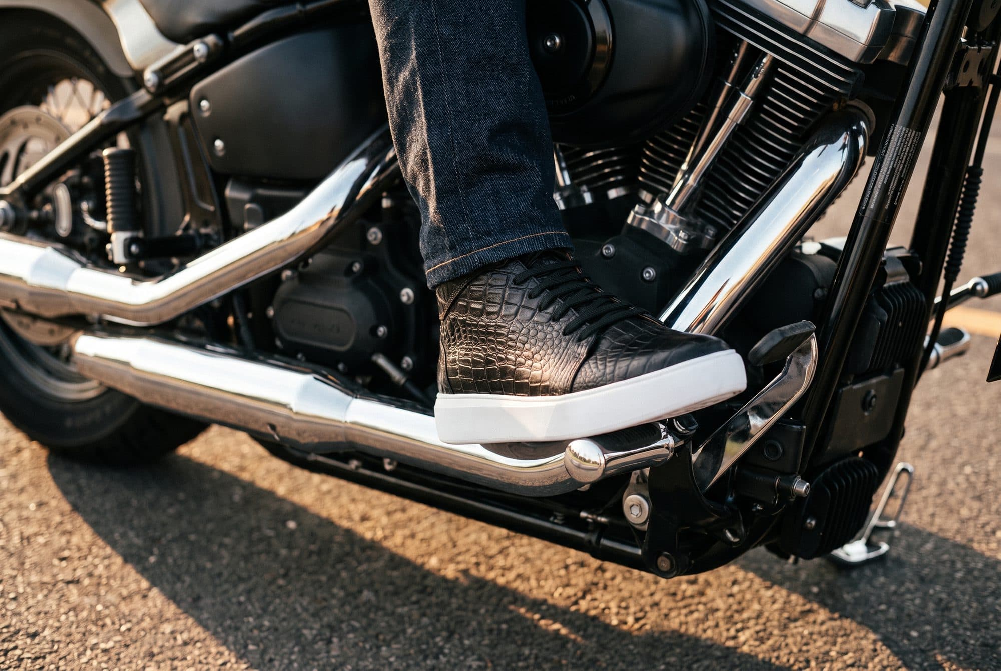 Sneaker de piel Blade con grabado cocodrilo apoyado en el estribo de una motocicleta al atardecer